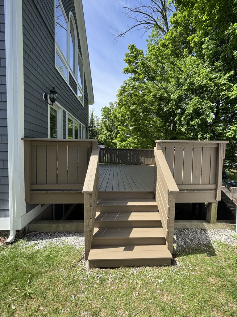 Elevated backyard deck refinished by Cramb Painting Co. in Pepperell MA, front view with stairs and brown stain