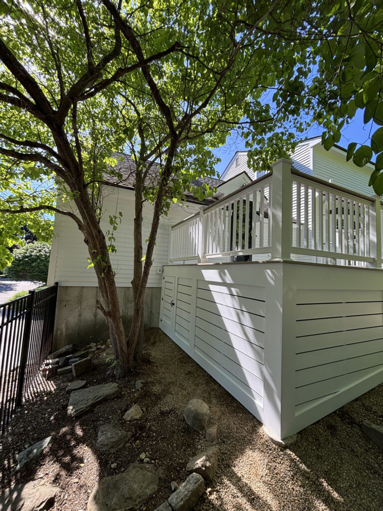Side view of elevated Hopkinton deck with white slatted skirting and freshly refinished railing by Cramb Painting Co.